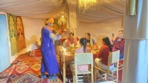 Travellers eating dinner in a Berber-style tent, served by a guide in a blue robe