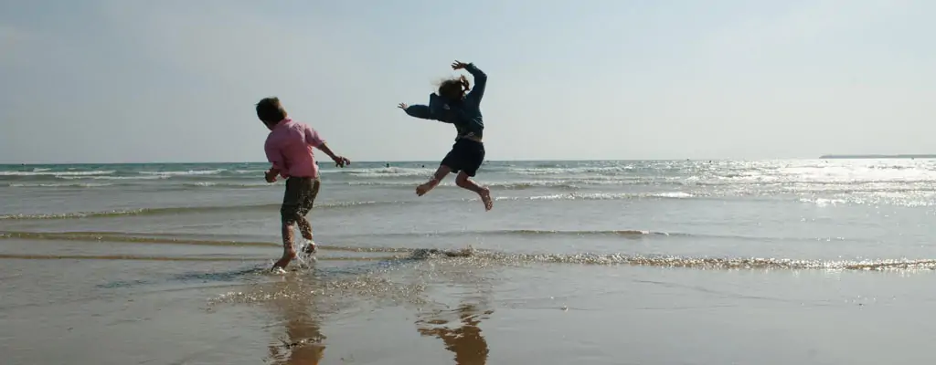 Two people playing at the edge of the sea on a sandy beach